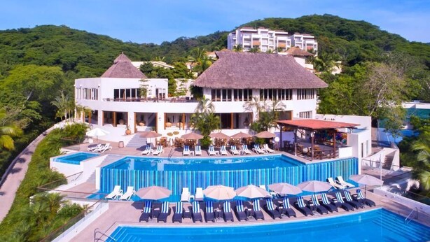 Un resort con una amplia piscina, sillas de descanso y un edificio con techo de paja.