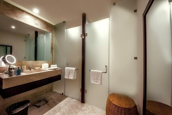 A modern bathroom with a large mirror, a vanity with toiletries, a shower area, and a wicker stool. - Grand Matlali Luxury Resort — Rooms Only | Mandatory All-Inclusive Paid at Resort. (Bucerias)