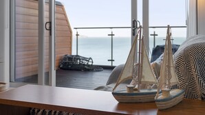 A balcony with a view of the sea, a wooden table with a model sailboat, and a patterned cushion. - Avocet 2 is a stylish coastal apartment offering uninterrupted sea views (Brixham)
