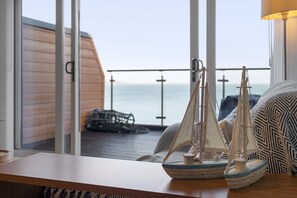 Ein Balkon mit Meerblick, ein Holztisch mit einem Modellsegelboot und ein gemustertes Kissen.