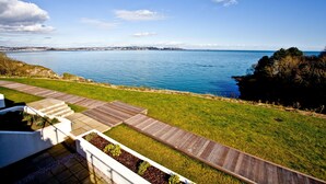 A coastal view with a grassy area, wooden deck, and a clear blue sky. - Avocet 2 is a stylish coastal apartment offering uninterrupted sea views (Brixham)