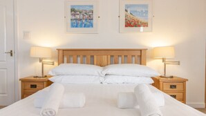 Ein ordentlich bezogenes Bett mit weißen Laken, zwei Nachttische mit Lampen und zwei gerahmte Bilder an der Wand.