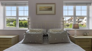 Une chambre à coucher comprenant un lit, deux tables de chevet, une commode, une fenêtre avec des stores et un tableau encadré accroché au mur.