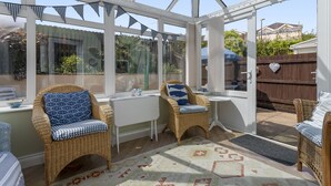 Une véranda meublée de mobilier en osier, agrémentée d’un tapis à motifs et offrant une vue sur l’extérieur.