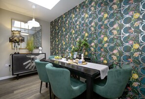 Un comedor con una mesa preparada para cuatro personas, un espejo sobre la mesa y un papel tapiz estampado.