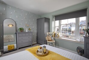 Un dormitorio con cama, cómoda, espejo, ventana con vista a barcos y cómoda con espejo.