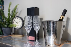 A table with two champagne flutes, a champagne bottle in a metal bucket, a clock, and a potted plant. - Five - La Petite Maison is a stylish waterfront holiday apartment in Brixham (Brixham)