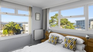 Quarto com cama, duas almofadas, mesa de cabeceira, abajur, janela e vista para o exterior.