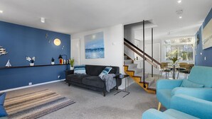 Uma sala de estar moderna com um sofá, uma mesa de centro e uma escada que leva a uma área de jantar.