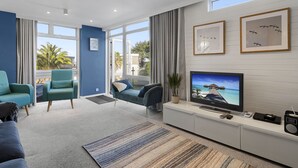 Sala de estar moderna com televisão, assentos e vista através de amplas janelas.