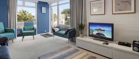 Una sala de estar moderna con televisor, asientos y vistas amplias por las ventanas.
