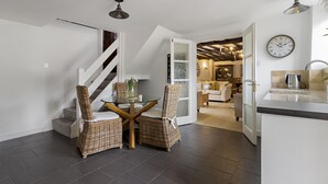 Une cuisine moderne dotée d’une cuisinière intégrée, un coin repas avec des chaises en osier et une table en verre, et un escalier menant à un autre niveau.