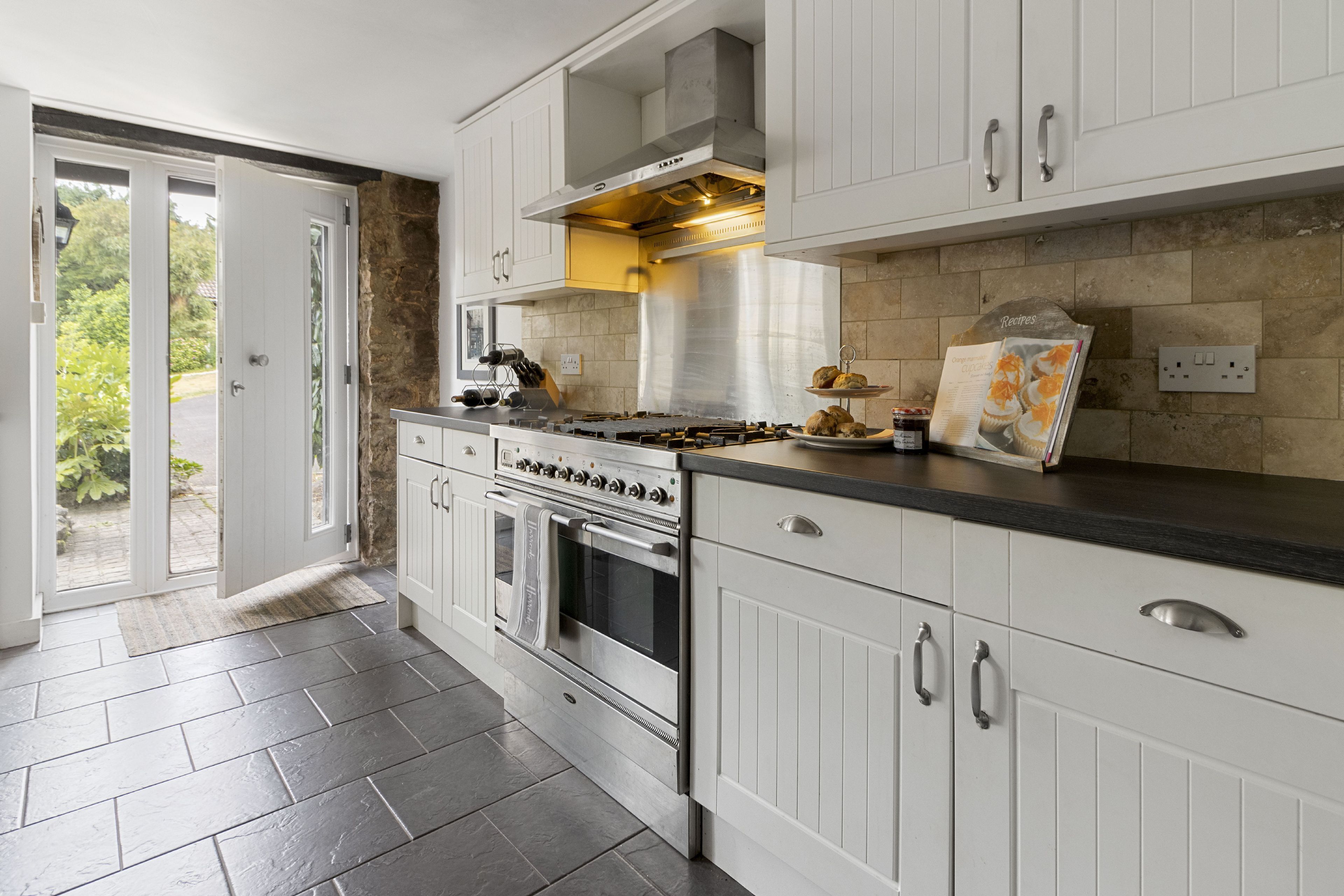 A modern kitchen with white cabinetry, a stainless steel range hood, and a stone backsplash.