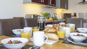 Ein Frühstückstisch mit Croissants, Früchten und Kaffee in einer modernen Küche.