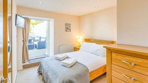 Ein Schlafzimmer mit einem Bett, einer Holzkommode, einem Fernseher und einem Fenster mit Vorhängen.