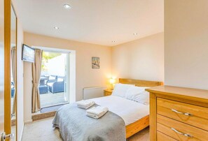 A bedroom with a bed, a wooden dresser, a television, and a window with curtains. - Anzac is a spacious four-bedroom holiday home in Brixham (Brixham)
