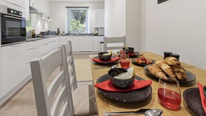 Una cucina moderna con mobili bianchi, un tavolo da pranzo apparecchiato con piatti, ciotole e un bicchiere di bevanda rossa.