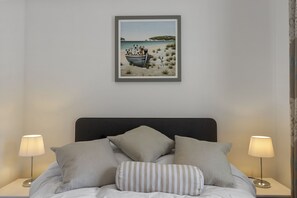 A bedroom with a bed, pillows, a framed picture on the wall, and two bedside lamps. - Harbour Reach is a charming and cosy two-bedroom holiday home in Brixham (Brixham)