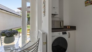 A compact laundry room with a washing machine, a drying rack, and a small countertop with jars. - Harbour Reach is a charming and cosy two-bedroom holiday home in Brixham (Brixham)