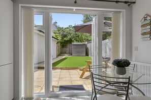 A glass door leading to a patio with a table and chairs, a small garden, and a wooden fence. - Harbour Reach is a charming and cosy two-bedroom holiday home in Brixham (Brixham)