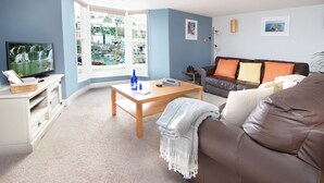 A living room with a television, a sofa, a coffee table, and a window with a view of buildings. - High Hopes, a stunning Grade II listed Brixham holiday cottage (Brixham)