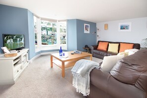 A living room with a television, a sofa, a coffee table, and a window with a view of buildings. - High Hopes, a stunning Grade II listed Brixham holiday cottage (Brixham)