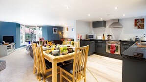 A modern kitchen with a dining area, featuring a wooden table and chairs, a built-in oven, and a view through a large window. - High Hopes, a stunning Grade II listed Brixham holiday cottage (Brixham)
