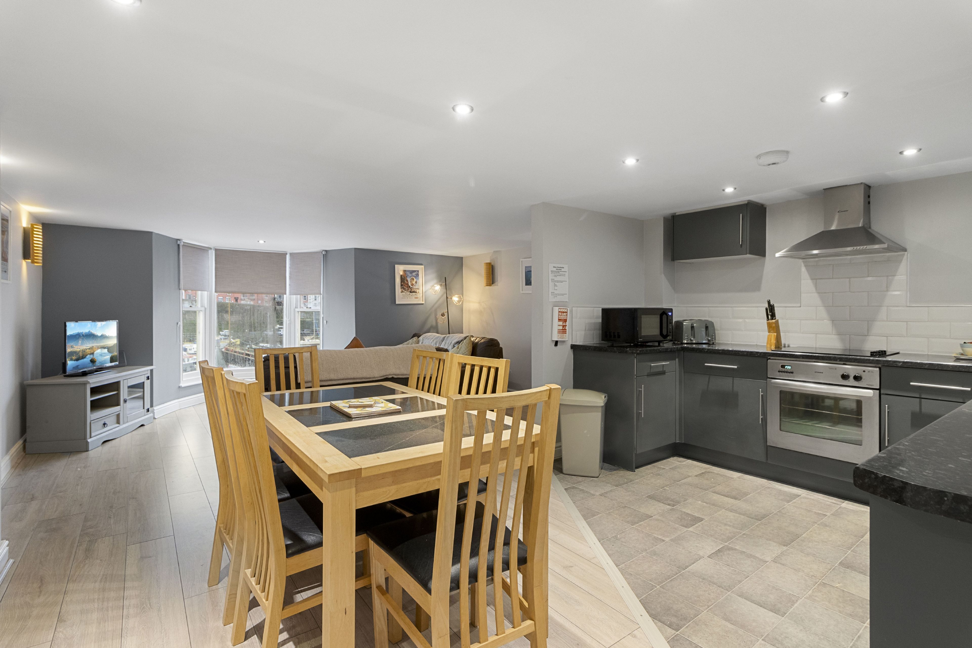 A modern kitchen with grey cabinets, a stainless steel oven, and a dining area with a wooden table and chairs.