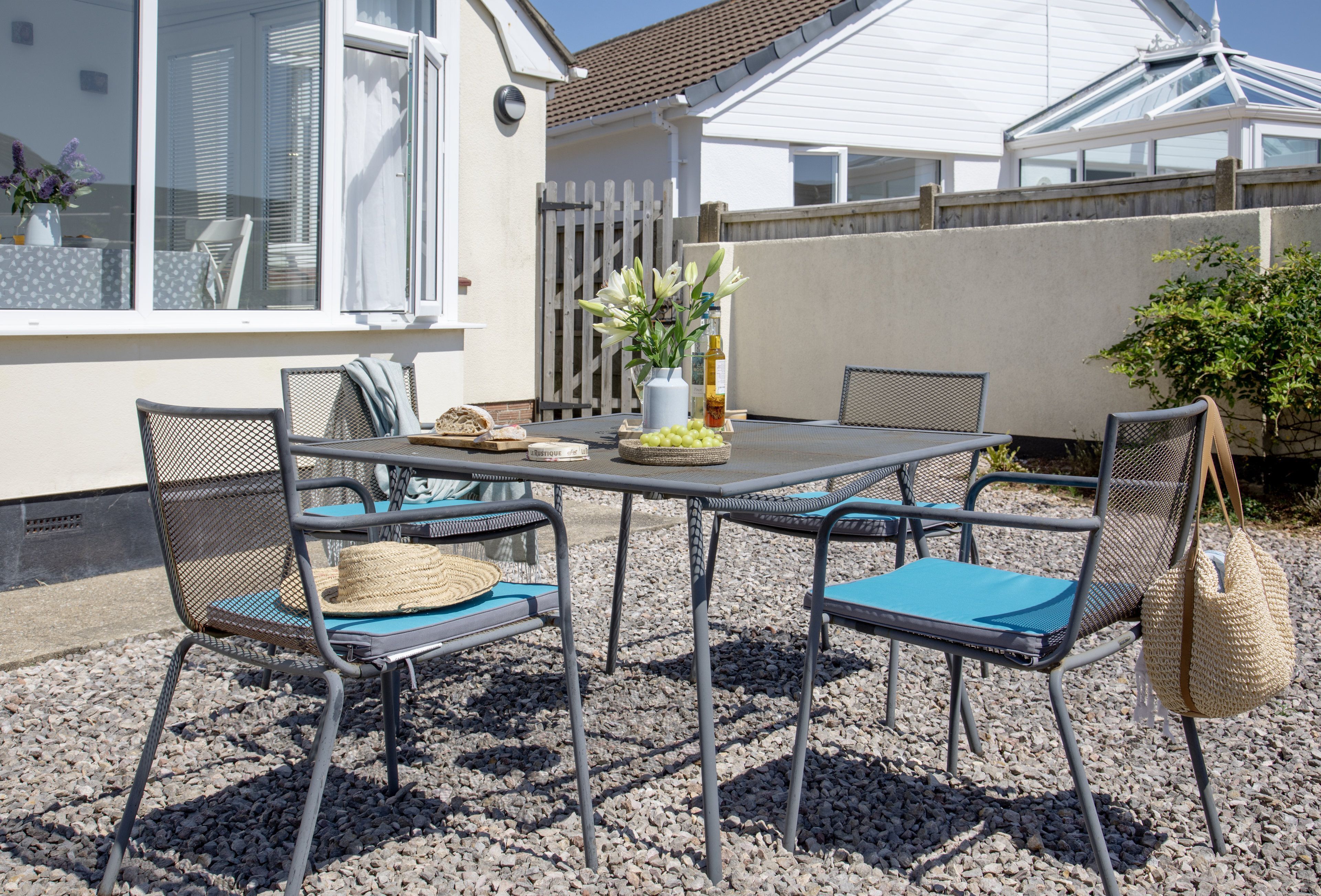 A patio with a table and chairs, a vase with flowers, and a fence in the background.