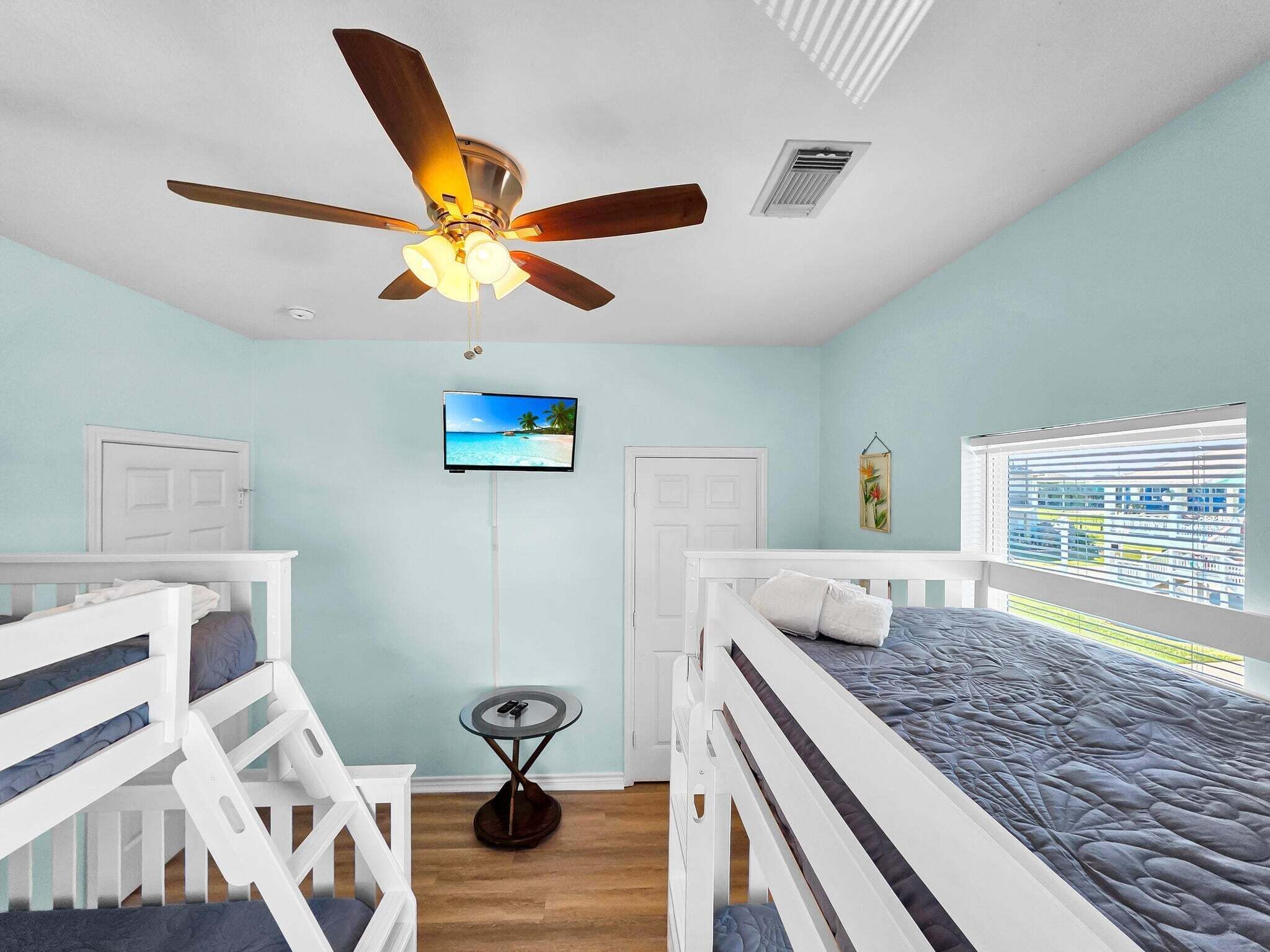 Ein Schlafzimmer mit Etagenbetten, Deckenventilator, Fernseher und einem Fenster mit Jalousien.