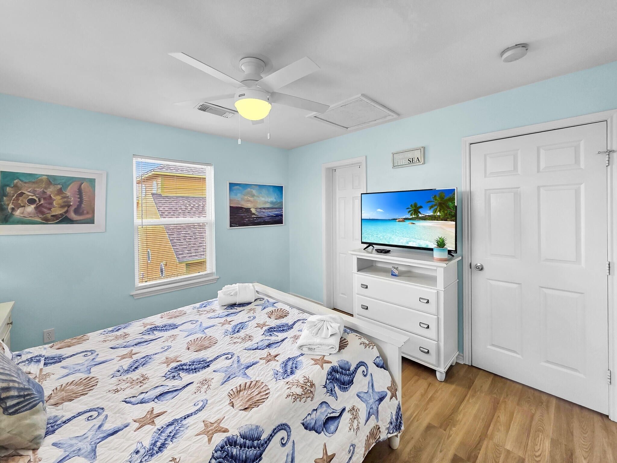 A bedroom with a bed, a ceiling fan, a TV, and a door.