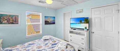 A bedroom with a bed, a ceiling fan, a TV, and a door.