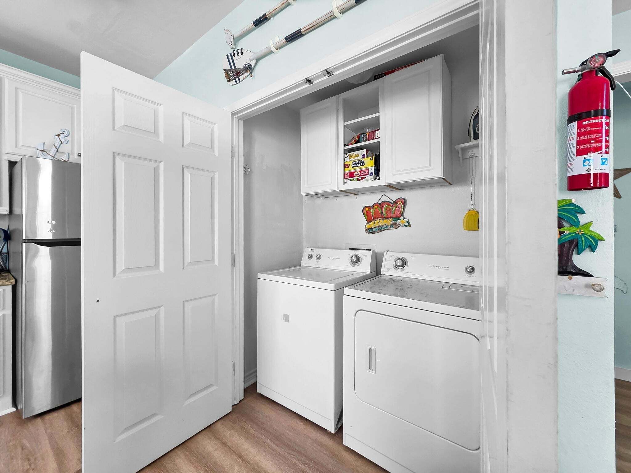 A compact kitchen with a refrigerator, two washing machines, and a fire extinguisher.