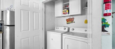 A compact kitchen with a refrigerator, two washing machines, and a fire extinguisher.
