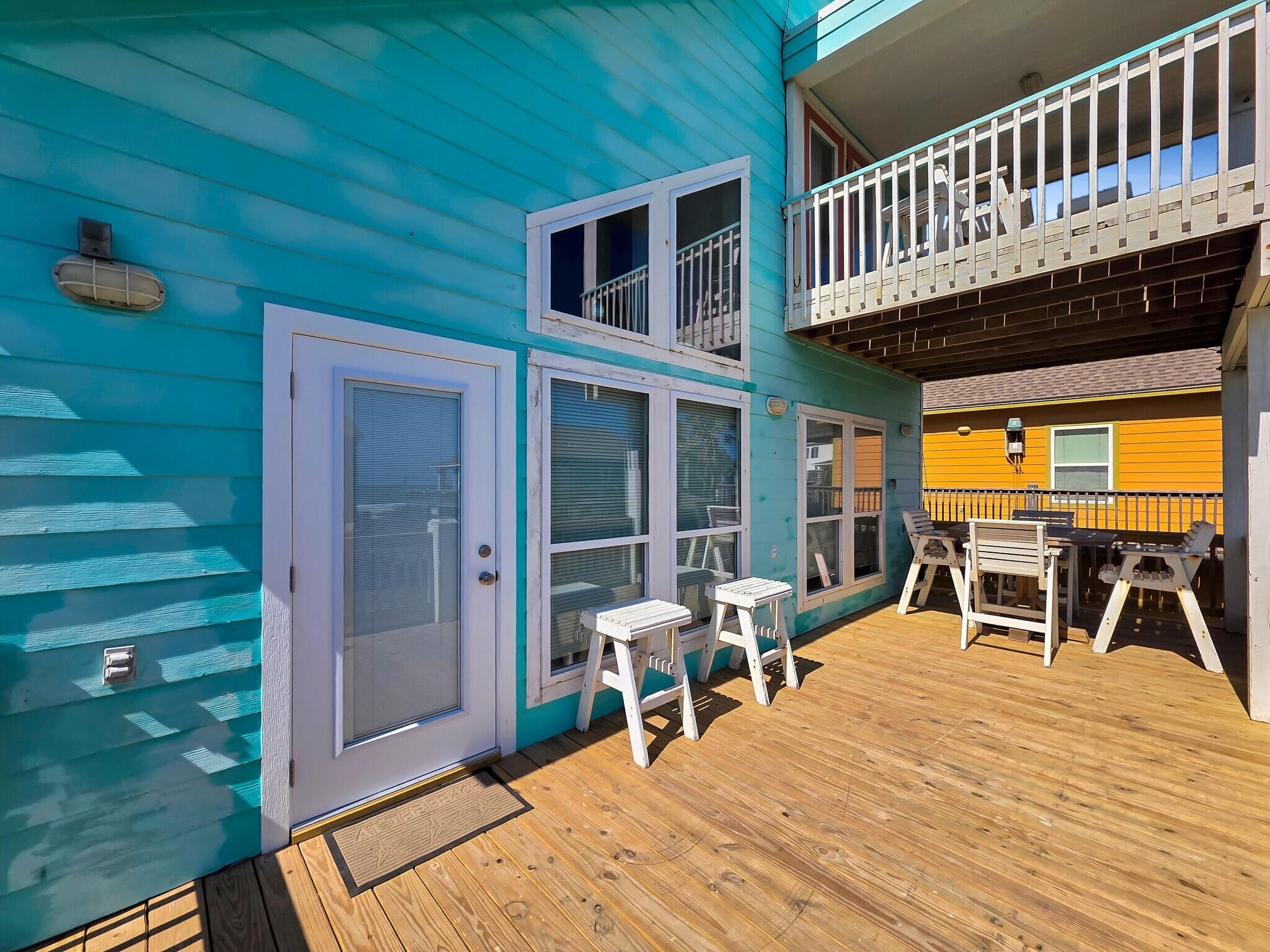 A two-story building with a balcony, a door with a screen, and a small outdoor seating area with tables and chairs.