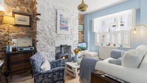 A cozy living room with a stone wall, a fireplace, a television, and a comfortable sofa. - Hope Cottage, a charming 1850s fisherman's cottage in Brixham (Brixham)