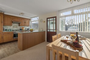 A kitchen with wooden cabinets, a central island, and a dining table with chairs. - Baywatch Sea View Retreat a beautifully refurbished coastal holiday home (Brixham)