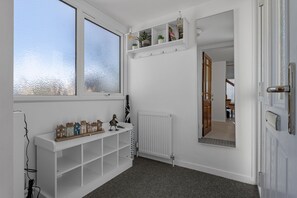 A hallway with a white radiator, a shelf with small plants, a mirror, and a window with frosted glass. - Baywatch Sea View Retreat a beautifully refurbished coastal holiday home (Brixham)