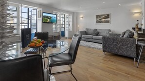 A modern living room with a glass dining table, a grey sofa, and a flat-screen TV. - Harbour Lights Apartment, a coastal retreat set on Torquay's vibrant marina (Torquay)