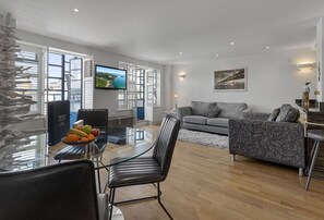 Ein modernes Wohnzimmer mit einem Glastisch, einem grauen Sofa und einem Flachbildfernseher.