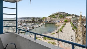 A balcony with a view of a marina, a promenade, and a hilltop building with a clock tower. - Harbour Lights Apartment, a coastal retreat set on Torquay's vibrant marina (Torquay)