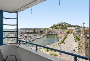 Ein Balkon mit Blick auf einen Yachthafen, eine Uferpromenade und ein Hügelgebäude mit einem Glockenturm.