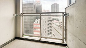 A window with a metal guard, a concrete wall, and a view of a cityscape with buildings. - Trioni EBISU  (Osaka)