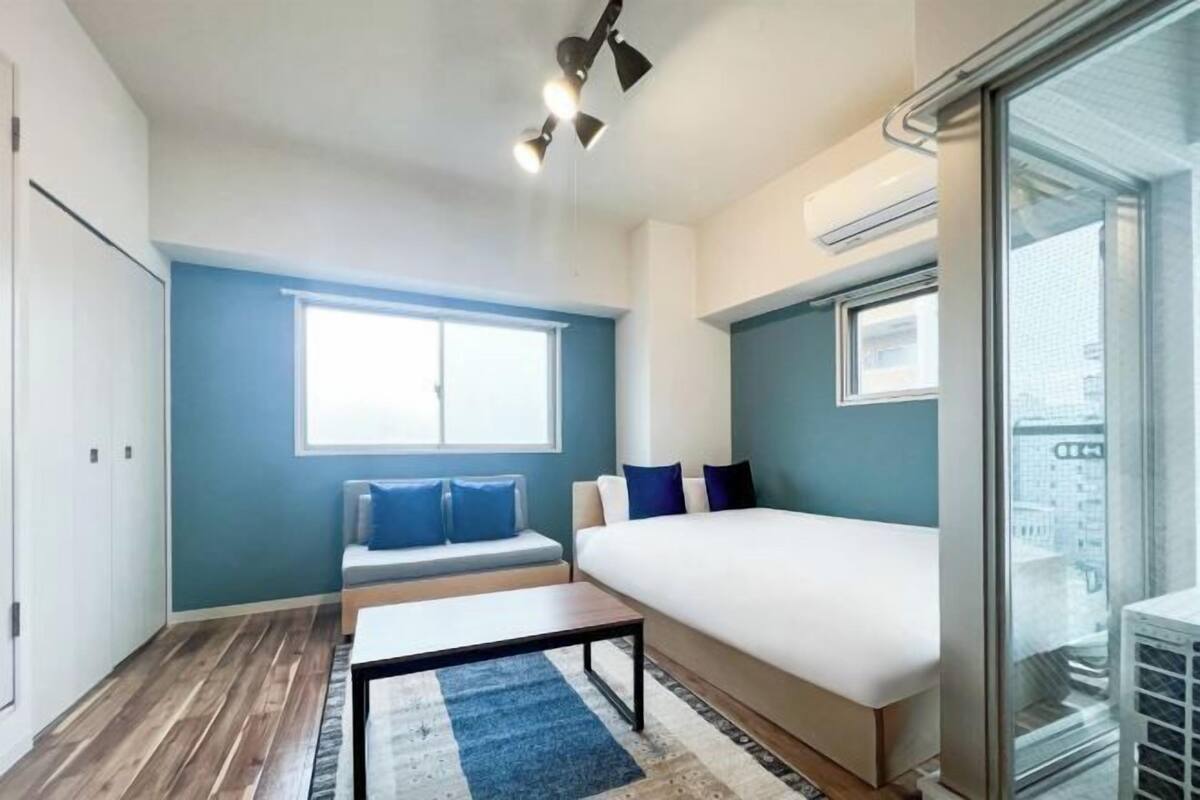 Une chambre d’hôtel moderne dotée d’un grand lit, d’un coin salon avec un canapé et des coussins, d’une petite table et d’une grande fenêtre offrant une vue sur la ville.