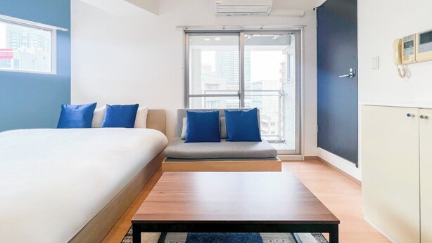 A hotel room with a bed, a sofa, a table, and a view of the city through a large window. - Trioni EBISU  (Osaka)