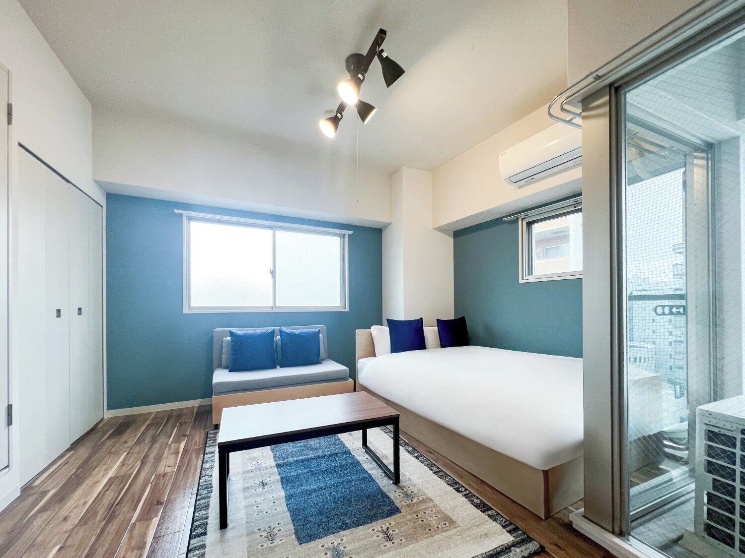 A bedroom with a bed, a sofa, a table, and a window.
