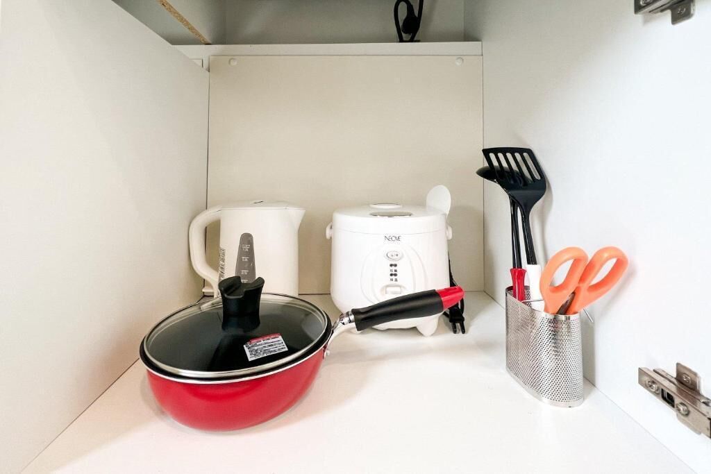 A kitchen with a red pot, a white rice cooker, and kitchen utensils.