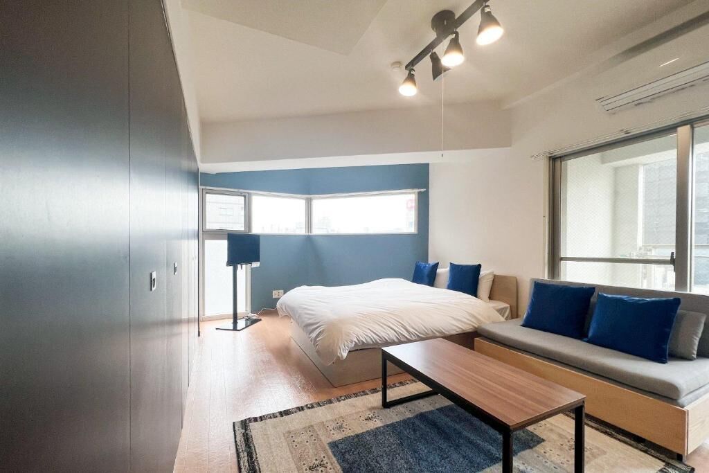 A modern bedroom with a bed, a sofa, a desk, and a large window.