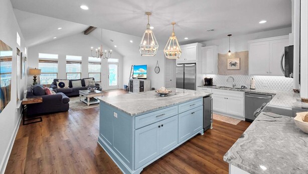 A spacious living area with a large island, a kitchen with white cabinets, and a dining area with a view. - Pearly Pelican 3 Bedroom Home (Port Bolivar)