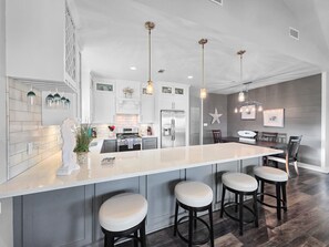 Una cocina moderna con una isla central, taburetes de bar, iluminación colgante y un comedor con un adorno de estrella en la pared.